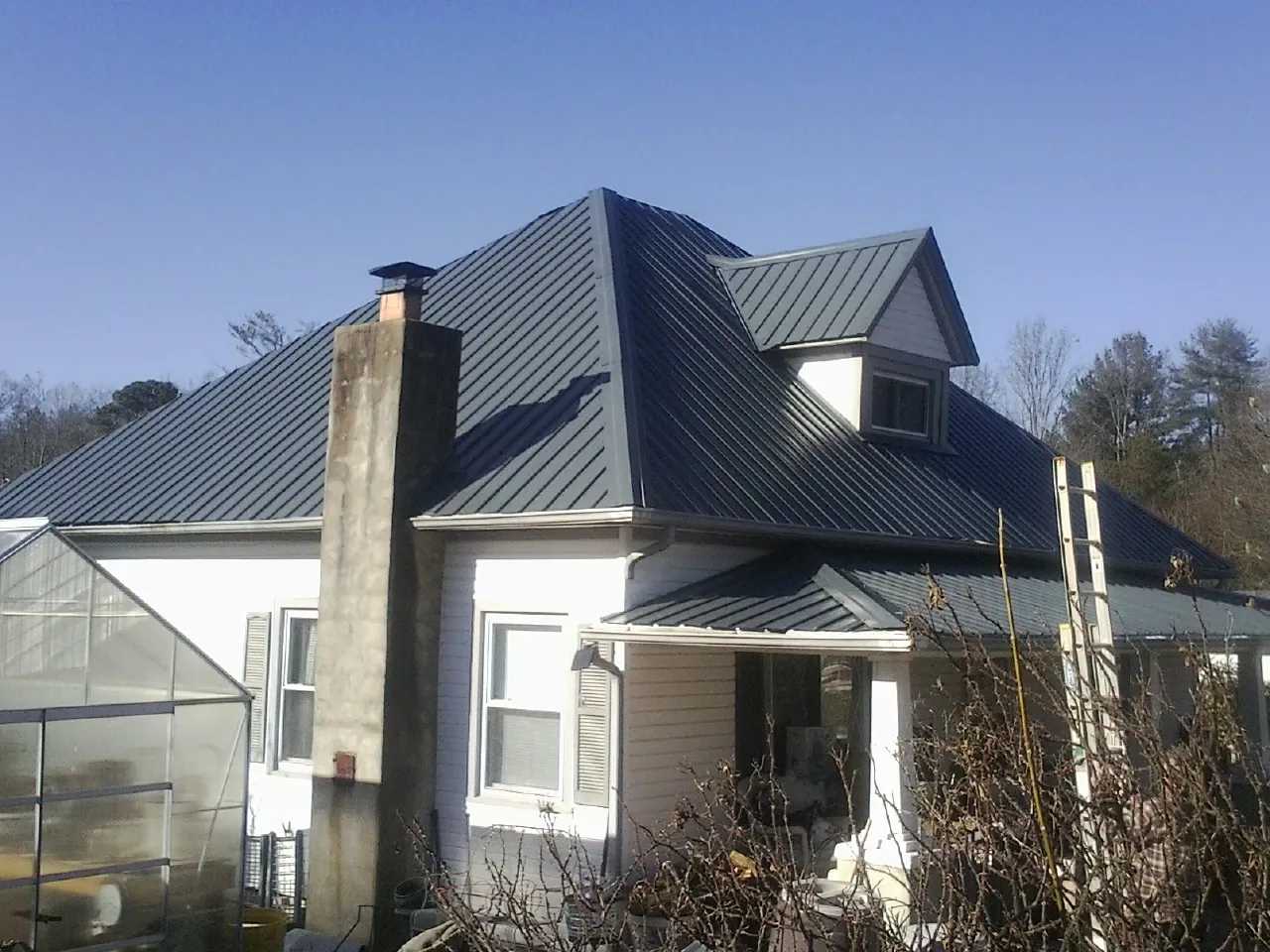 Dark blue standing seam metal roof on a white farmhouse with dormer — Slate & Tile Roof Repair by Roofing Brothers in Culdesac