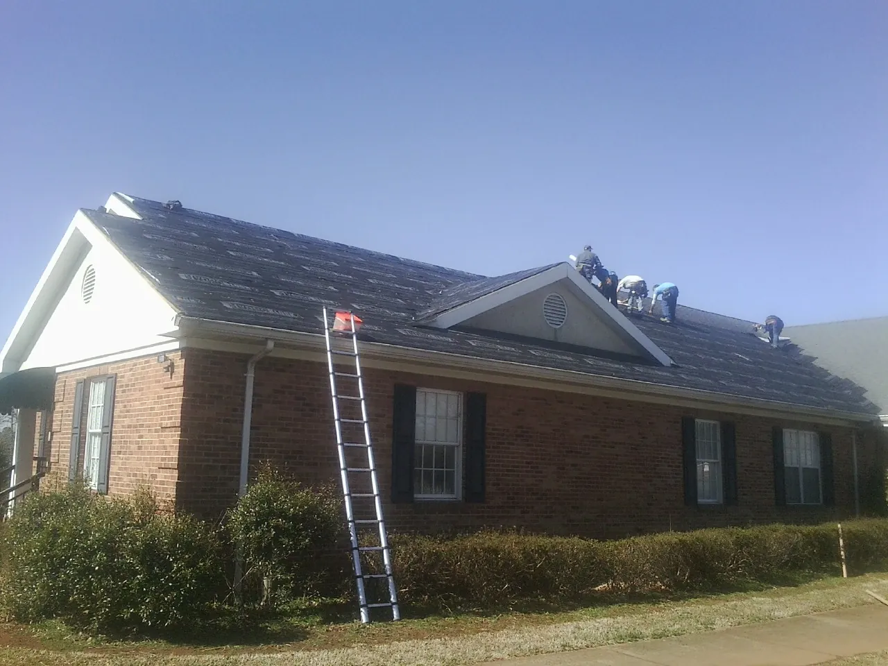 Crew tearing shingles off a brick ranch roof with a ladder set — Metal Roof Repair work by our crew in Culdesac