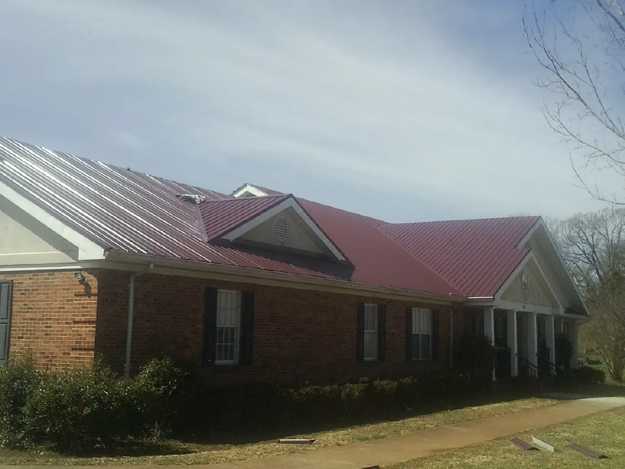 Red metal roof with gabled entries on a long brick building, from a Hail Damage Roof Repair job in Culdesac