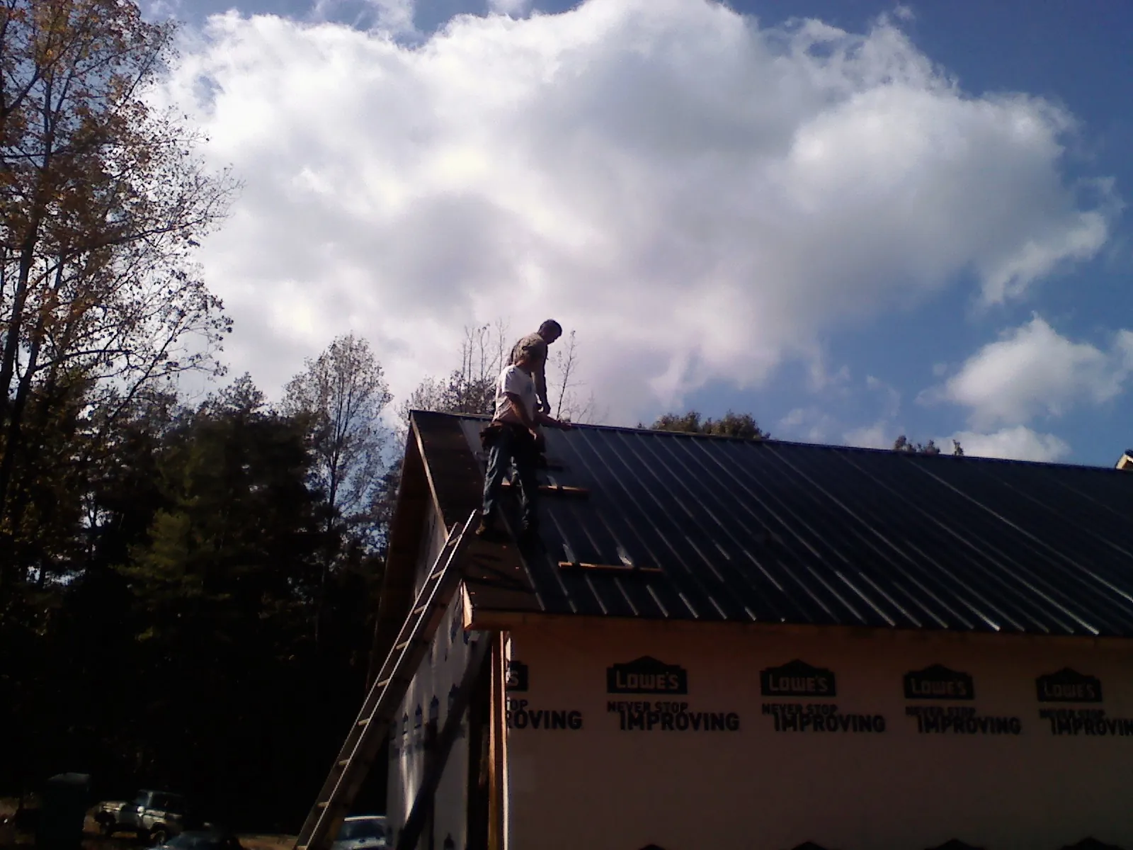 Roofer fastening dark metal panels high against a cloudy sky, from a Roof Inspection job in Culdesac