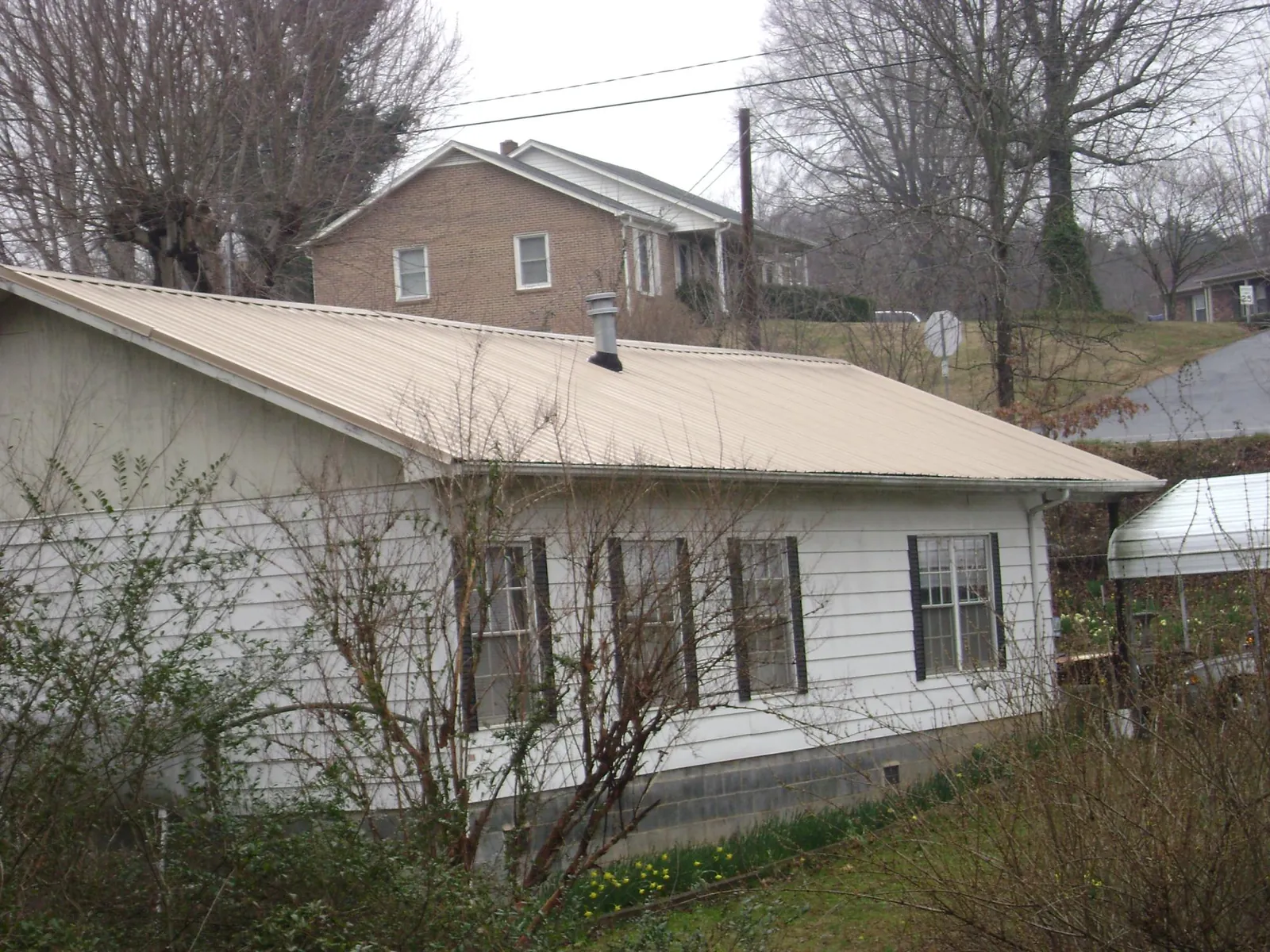 Tan metal roof on a white sided house set into a hillside — Commercial Roofing by Roofing Brothers in Culdesac